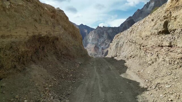 Aerial view of a dirt road cutting through rugged rocky terrain with prayer flags strung across the path in Zanskar, Ladakh, India.