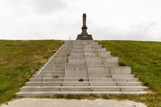 View of the De Man monument standing atop a stone staircase built into a grassy dike, featuring historical flood dates engraved on the steps in Harlingen, Friesland, Netherlands.