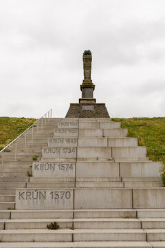 View of the De Man monument, a stone pillar atop a staircase on a grassy dike, featuring historical dates engraved on the steps, in Harlingen, Friesland, Netherlands.