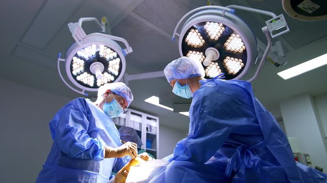 Team of surgeons stand at the operating table under the round lamps. Doctors perform surgery on trauma.
