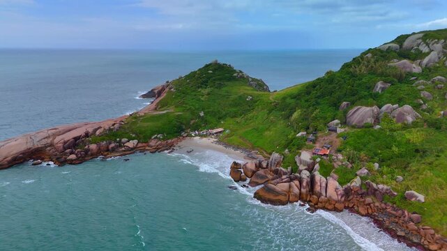 Aerial view of Praia do Gravata featuring rocky cliffs, lush green hills, and turquoise ocean waters along the coastline in Florianopolis, Santa Catarina, Brazil.