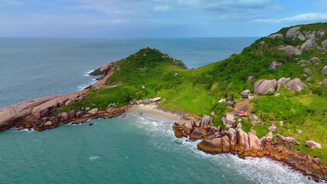 Aerial view of Praia do Gravata featuring rocky coastline, green hills, sandy beach, and turquoise ocean waters in Florianopolis, Santa Catarina, Brazil.