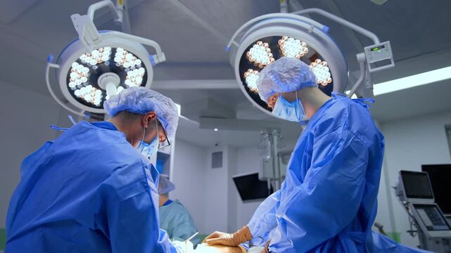 Modern surgery on trauma. Surgical team wearing blue uniforms work at the operating table under the round lamps.