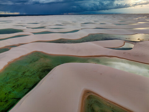 Aerial view of Lagoa Bonita featuring white sand dunes and vibrant turquoise lagoons under a dramatic dark storm sky in Barreirinhas, State of Maranhao, Brazil.