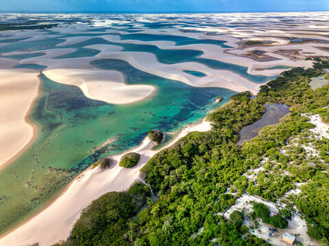 Aerial view of Parque Nacional dos Lencois Maranhenses featuring vast white sand dunes and turquoise lagoons surrounded by lush green vegetation in MA, Brazil.