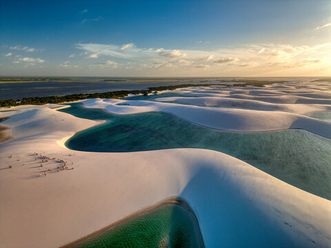 Aerial view of Parque Nacional dos Lencois Maranhenses with white sand dunes and turquoise lagoons under golden hour light in MA, Brazil.