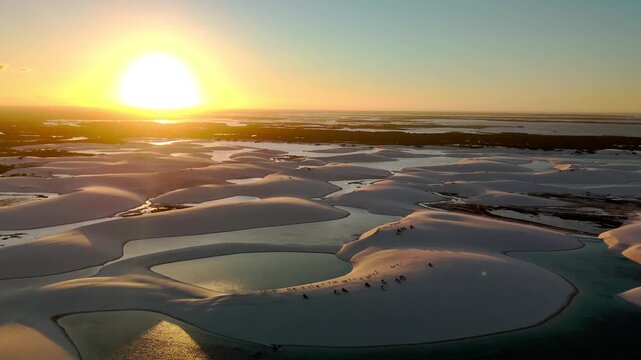 Aerial view of Parque Nacional dos Lencois Maranhenses featuring white sand dunes and turquoise lagoons under a golden sunset in MA, Brazil.