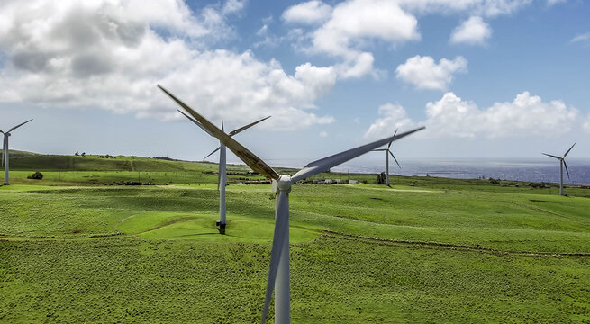 Aerial view of Hawi Renewable Development Wind Farm with large white wind turbines set against lush green rolling hills and the Pacific Ocean in Hawi, Hawaii, United States.
