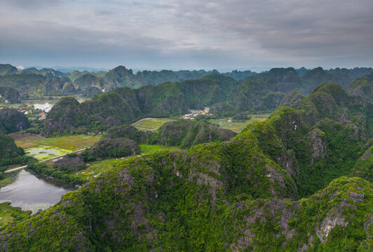 Aerial view of Tam Coc - Bich Dong limestone karst mountains with lush green vegetation, winding river, and agricultural fields in Nam Hoa Lu, Ninh Binh, Vietnam.