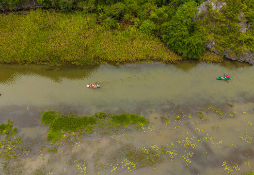 Aerial view of small boats navigating the green river through the limestone karst formations of Tam Coc - Bich Dong in Nam Hoa Lu, Ninh Binh, Vietnam.