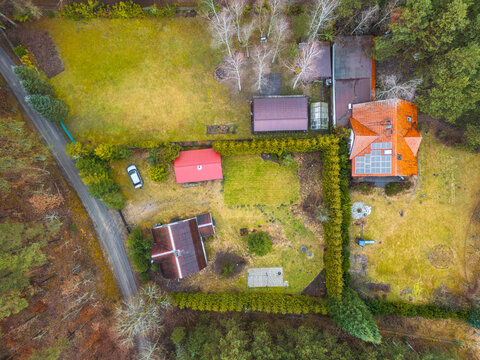 Aerial view of a residential property with solar panels on a red roof, a car parked in the yard, and a large hedge, surrounded by a forest in Zawada, Pomeranian Voivodeship, Poland.