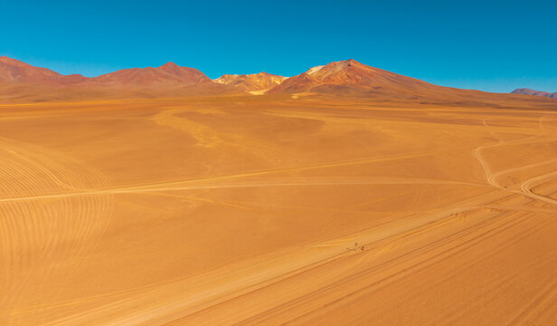 Aerial view of the Arbol de Piedra rock formation in the arid desert landscape with tire tracks on the sandy ground and distant mountains under a clear blue sky in Juntacha, Potosi, Bolivia.