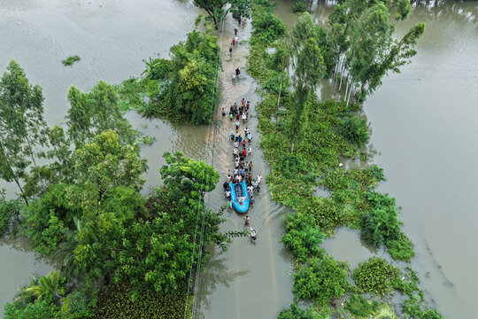 Banshkhali Upazila, Chittagong Division, Bangladesh - 10 July 2026: Aerial view of people wading through floodwaters and using a small boat to navigate a submerged road.
