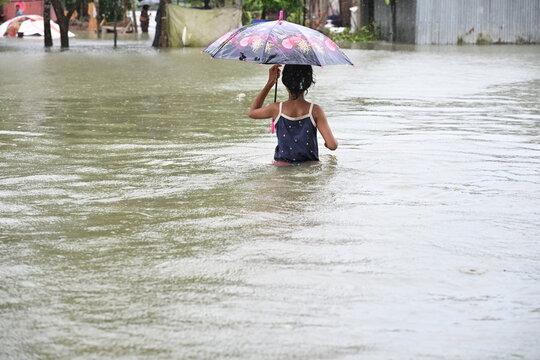 Banshkhali Upazila, Chittagong Division, Bangladesh - 10 July 2026: View of a young person wading through floodwaters while holding an umbrella in a flooded residential area.