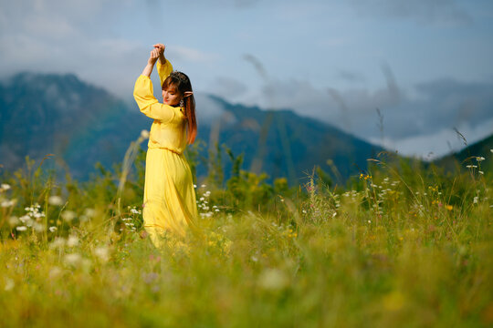 Young elf female dancing in yellow dress amidst mountainous wildflower field