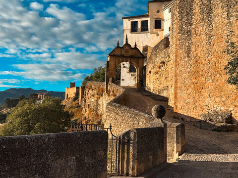 View of the historic stone archway and ancient fortifications in the old town of Ronda, with warm sunlight on the textured masonry and blue sky in Ronda, Andalusia, Spain.