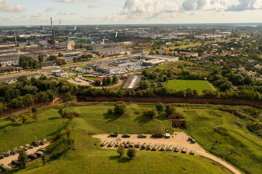Aerial view of military vehicles parked at the historic Kaunas Fortress fortifications with an industrial urban landscape in the background in Kelme, Kaunas County, Lithuania.