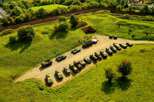 Aerial view of a collection of military tanks and armored vehicles parked in a row on a gravel path within a historic grassy fortification in Kelme, Kaunas County, Lithuania.