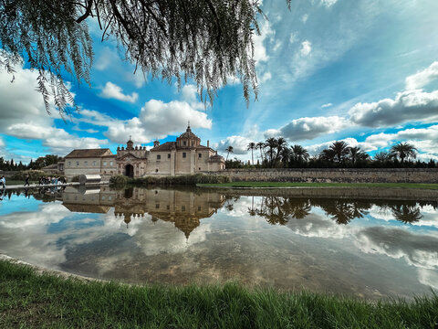 Seville, Spain - 02 November 2025: View of the historic Monasterio de la Cartuja reflecting in calm waters under a bright blue sky with scattered clouds in Seville, Andalusia, Spain.