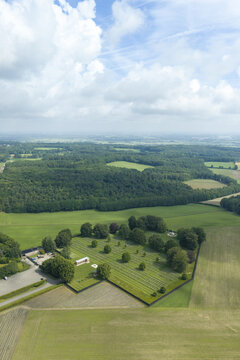 Aerial view of the Groesbeek Canadian War Cemetery with rows of white headstones set in lush green grass surrounded by trees and agricultural fields in Groesbeek, Gelderland, Netherlands.