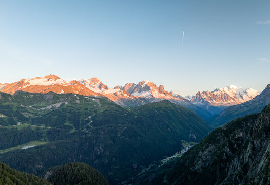 Aerial view of the snow-capped peaks of the Mont Blanc massif illuminated by the golden morning light above the lush green valleys near Finhaut, Valais, Switzerland.