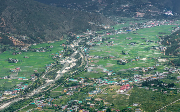 Aerial view of the lush green Paro Valley with its winding river, traditional houses, and terraced rice fields nestled among the Himalayan mountains in Paro, Paro, Bhutan.
