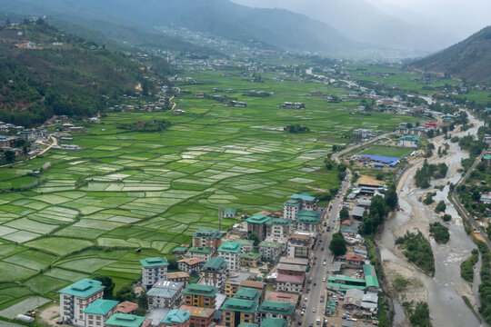Aerial view of Paro Valley View Point featuring vibrant green rice fields, traditional buildings, and a winding river in Paro, Paro, Bhutan.
