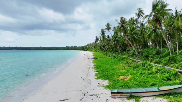 Aerial view of Pantai Ohoidertutu Ngur Mun Vat Wahan with white sand beach, turquoise water, palm trees, and wooden boats in Kei Kecil Barat, Maluku, Indonesia.