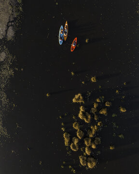 Aerial view of colorful kayaks paddling through the dark waters of the Xochimilco canals surrounded by aquatic vegetation in Xochimilco, Mexico City, Mexico.