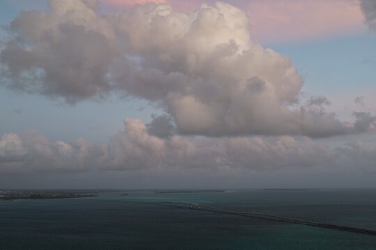 Aerial view of Irabu Bridge spanning the turquoise waters of the East China Sea under a dramatic cloudy sky in Miyakojima, Okinawa, Japan.