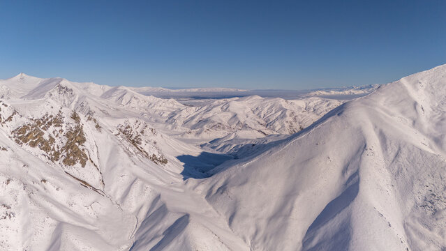 Aerial view of the snow-covered peaks and rugged terrain of Lindis Pass in the Otago Region, New Zealand.