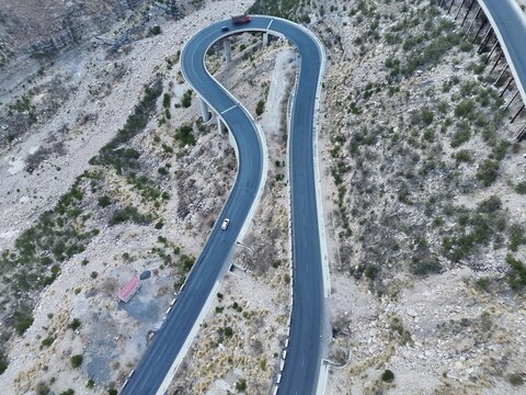Aerial view of the winding Steel Bridge at Fort Munro with vehicles driving along the curved asphalt road through the rugged mountainous terrain in Dera Ghazi Khan, Punjab, Pakistan.