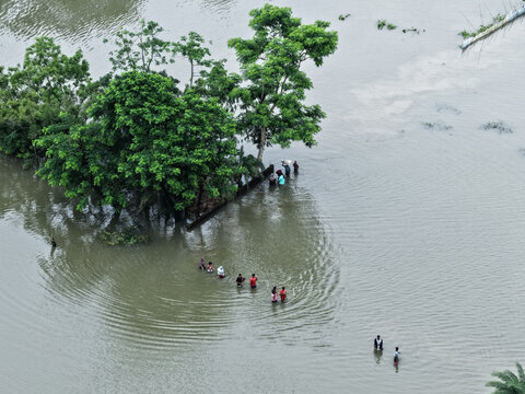 Banshkhali Upazila, Chittagong Division, Bangladesh - 10 July 2026: Aerial view of people wading through floodwaters in a submerged landscape with trees and murky water.