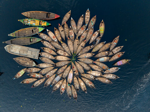 Aerial view of traditional wooden boats arranged in a circular pattern on the Buriganga River in Dhaka Division, Bangladesh.