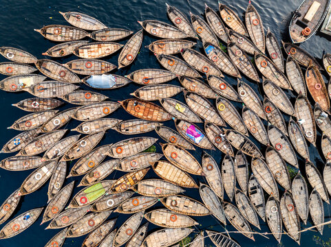 Aerial view of numerous wooden boats moored on the Buriganga River, showing the dense arrangement of vessels with lifebuoys and cargo in Dhaka Division, Bangladesh.
