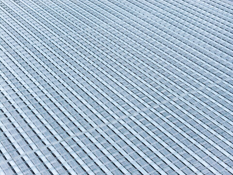 Aerial view of a large greenhouse roof with repeating glass panels and metal frames in Poland.