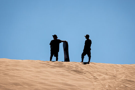 View of two people silhouetted against a clear blue sky while sandboarding on the dunes of Death Valley in San Pedro de Atacama, Antofagasta, Chile.