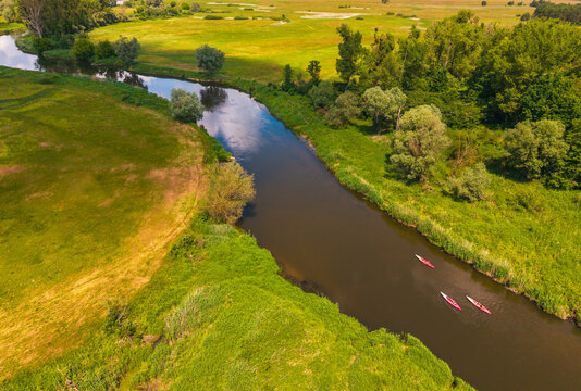 Aerial view of the Warta River winding through the lush green meadows of Nadwarcianski Park Krajobrazowy with three kayaks paddling downstream, Lad, Greater Poland Voivod, Poland.