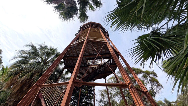 View of the historic Water Tower Lookout with its rusted metal structure and staircase framed by palm trees in Port Augusta West, South Australia, Australia.