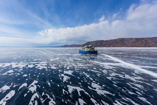 View of a hovercraft traveling across the frozen surface of Lake Baikal with intricate ice patterns and distant mountains under a clear blue sky in Listvyanka, Irkutsk Oblast, Russia.