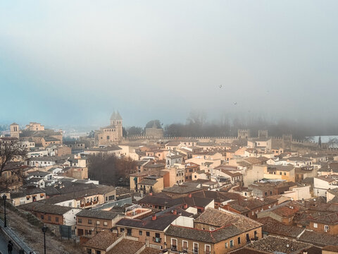 Toledo, Spain - 27 December 2025: View of the historic city of Toledo with its ancient stone fortifications and traditional rooftops under a misty sky.