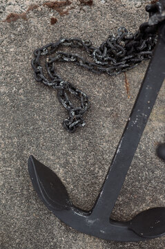 Close-up of a weathered black anchor and chain resting on a textured surface