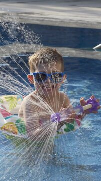 Little boy sprays water from colorful water blaster beside swimming pool. Active family leisure, outdoor recreation, playful summer activity and vacation concept. 