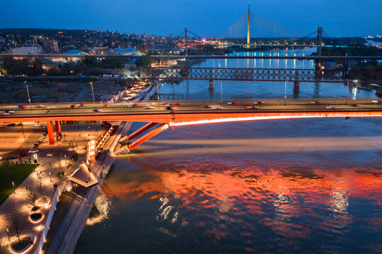 Aerial view of the illuminated Gazela Bridge and Ada Bridge spanning the Sava River at dusk with city lights reflecting on the water in Belgrade, City of Belgrade, Serbia.