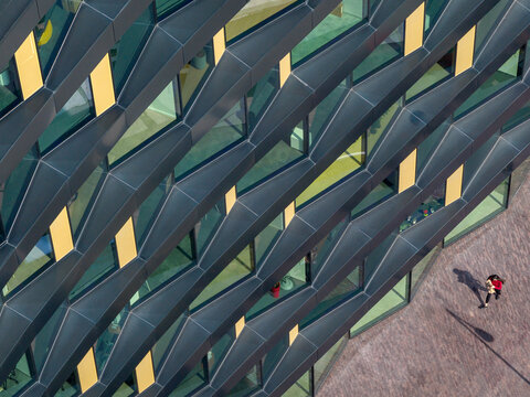Aerial view of the geometric facade of a modern office building with reflective glass panels and yellow accents, with a person walking on the ground in Belgrade, City of Belgrade, Serbia.