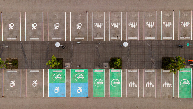 Aerial view of a parking lot with designated spaces for electric vehicles, families, and people with disabilities, marked with painted symbols on the pavement in Reykjavik, Iceland.