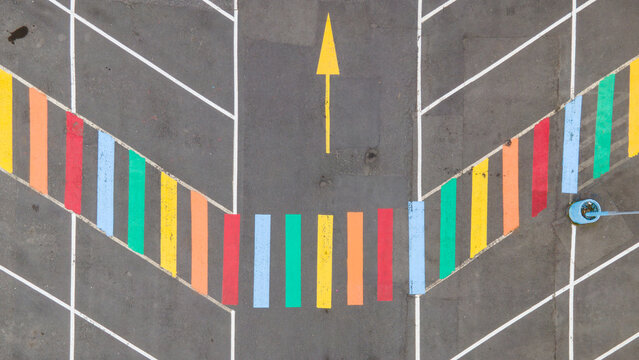 Aerial view of a parking lot featuring vibrant, multi-colored painted stripes and a yellow directional arrow on the asphalt surface in Reykjavik, Reykjavikurborg, Iceland.