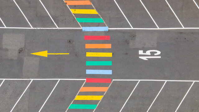 Aerial view of a colorful rainbow-painted pedestrian crossing in a parking lot with a yellow directional arrow and the number 15 painted on the asphalt in Reykjavik, Reykjavikurborg, Iceland.