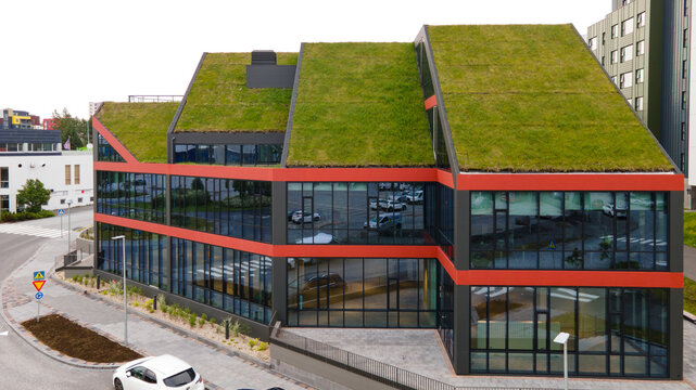 Aerial view of a modern building featuring a lush green roof, large glass windows, and striking red horizontal accents in Reykjavik, Reykjavikurborg, Iceland.