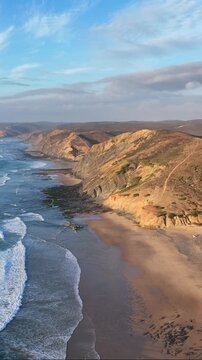Aerial view of Vale Figueiras Beach with golden sand, rugged cliffs, and Atlantic waves crashing on the shore in Bordeira, Faro District, Portugal.